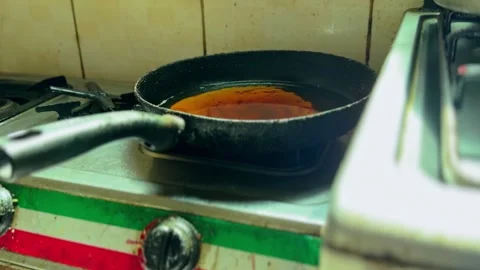 Cast iron pan with hot cooking oil on gas stove in rustic kitchen close up Stock Footage 332391036