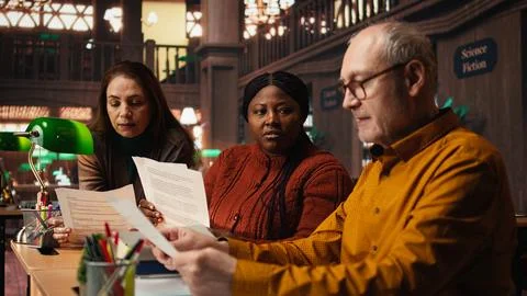 Cast members practicing script reading for a classic drama play in a library Stock Photos