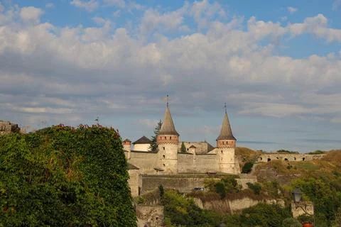 Castle stands on a hill under a cloudy sky with trees and stone walls around it Stock Photos