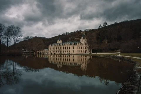 The castle is surrounded by dark clouds over water and in front of some rocks Foto stock
