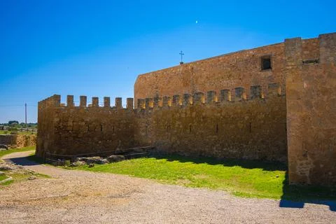 A castle wall with arrow slits protecting a simple square cathedral with a cr Stock Photos