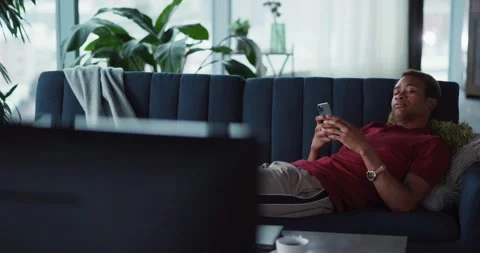 Casual afro-american young man resting down on couch using smartphone playing Stock Footage 148161353