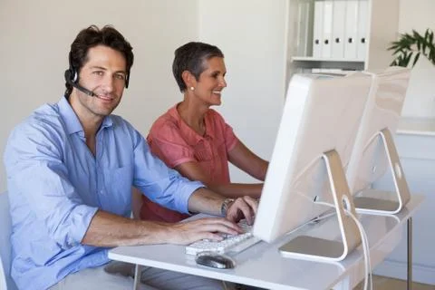 Casual business team working at desk using computers with man smiling at camera Stock Photos