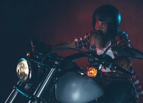 Casual cool long beard man with helmet riding motorcycle at night. Stock Photos