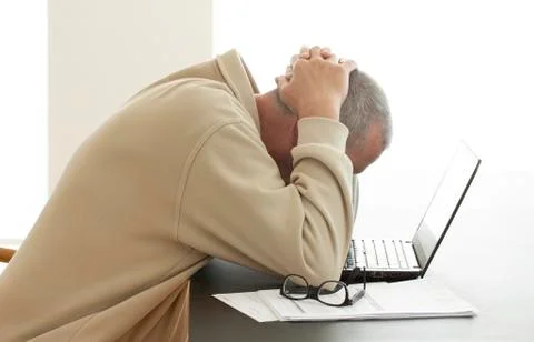 Casual dressed man bends his head over computer in despair Stock Photos