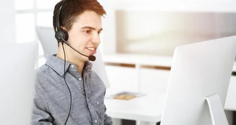 Casual dressed young man using headset and computer while talking with customers Stock Photos