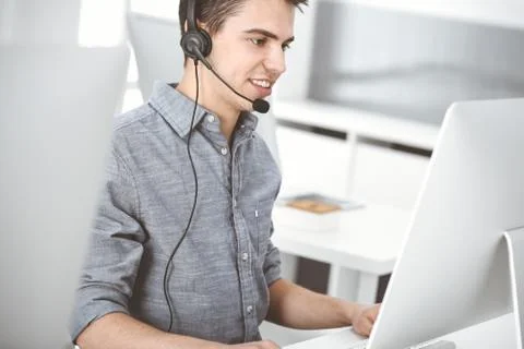 Casual dressed young man using headset and computer while talking with customers Stock-Fotos