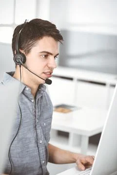 Casual dressed young man using headset and computer while talking with customers Foto stock