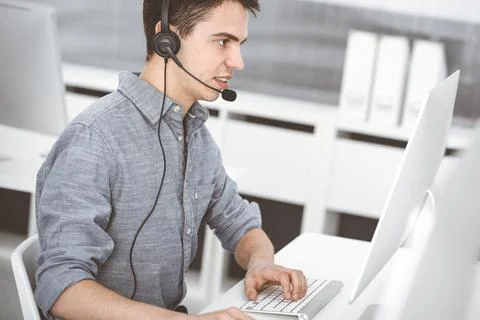 Casual dressed young man using headset and computer while talking with customers Stock Photos