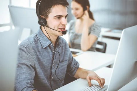Casual dressed young man using headset and computer while talking with customers Stock Photos