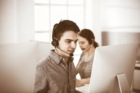 Casual dressed young man using headset and computer while talking with customers Stock Photos