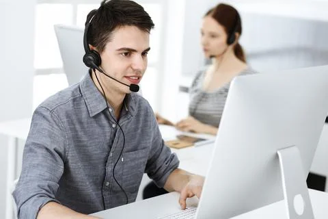 Casual dressed young man using headset and computer while talking with customers Stock Photos