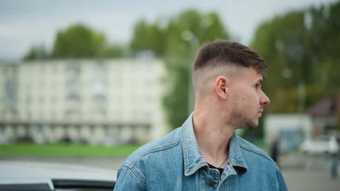 Casual driver under cloudy sky, Thoughtful young man in denim outdoors, Young Stock Footage 327729287
