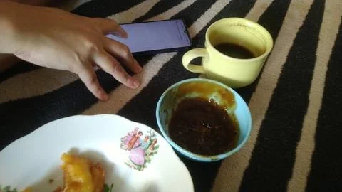 A casual hand uses a smartphone while enjoying coffee and a snack  Stock Photos