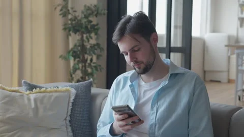 Casual Man Scrolling on Smartphone while Relaxing in Bright Modern Living Space Stock Footage 301241570