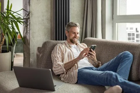 Casual man using phone in modern bright living room. Stock Photos