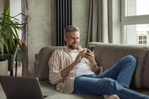 Casual man using phone in modern bright living room. Stock Photos
