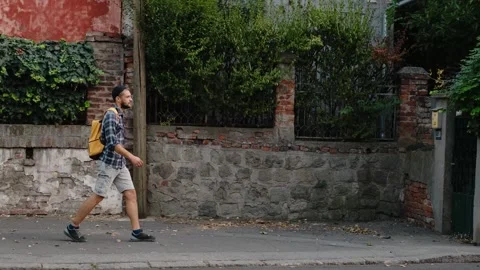 Casual man with a yellow backpack walks along an old brick and stone wall Stock Footage 342537610