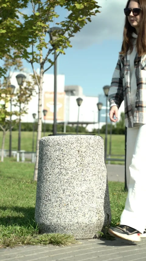 Casual person dropping garbage into public granite container amid green lawn Stock Footage 345527975