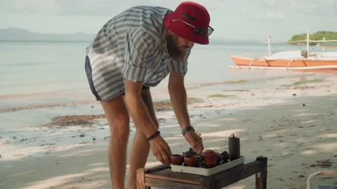 Casual shore side tea display. Man prepares portable tea set on shoreline Stock Footage 335637549