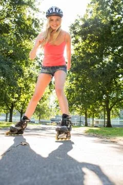 Casual smiling blonde inline skating on pathway Stock Photos