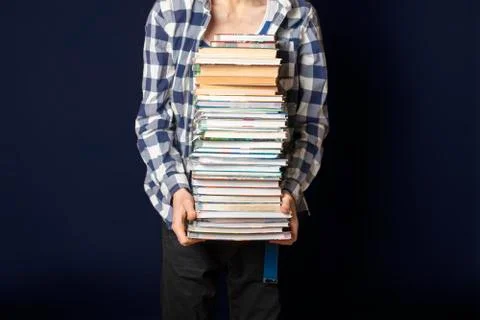 Casual student carry huge stack of books on dark background Stock Photos