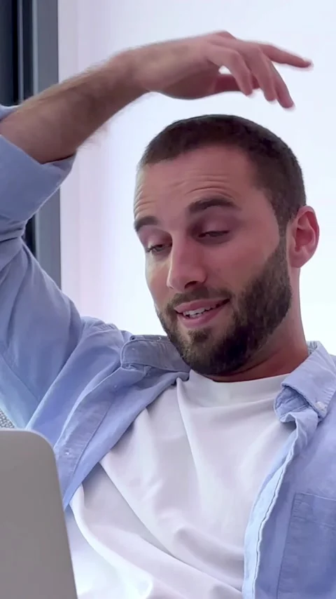 Casual young man with a beard sitting comfortably on a couch at home, actively Stock Footage 345117432