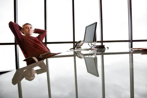 Casually dressed caucasian businessman relaxed at his reflective desk in front Stock Photos