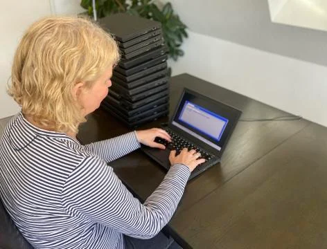 A casually dressed caucasian middle aged woman is installing a laptop computer Stock Photos