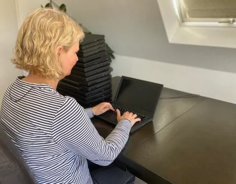 A casually dressed caucasian middle aged woman is installing a laptop computer Stock Photos