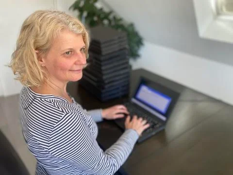 A casually dressed caucasian middle aged woman is installing a laptop computer Stock Photos