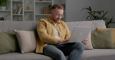 Casually dressed man sitting on cozy sofa while using laptop. Stock Footage 249465847