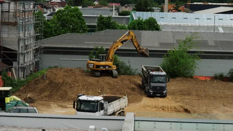 CAT excavator loading dump truck at active urban construction site Stock Footage 334689871
