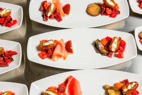 Caterer puts the starter on many plates with vegetables and antipasti Stock Photos
