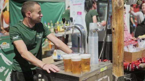 Caterer serves cold draught lager beer from festival bar on sunny day Stock Footage 193368475