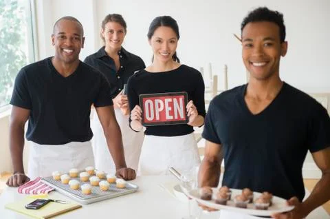 Caterers smiling together with food and open sign in event space Stock Photos