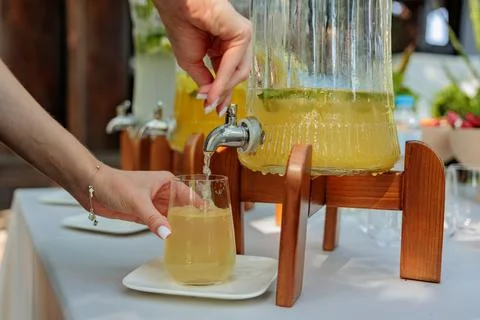 A catering waiter is skillfully pouring refreshing lemonade from a glass jar  Stock Photos