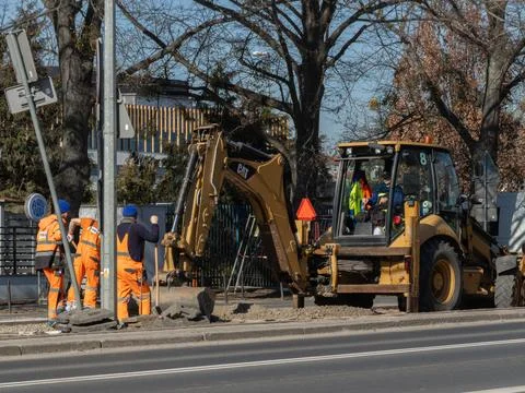 Caterpillar backhoe loader operator and construction workers performing road Stock Photos