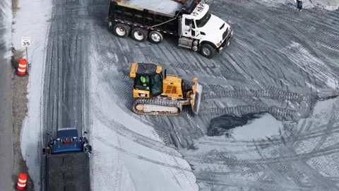 Caterpillar dozer spreading stone beside a dump truck Stock Footage 346167389