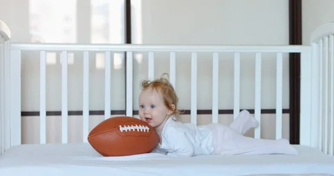Caucasian baby playing with American football ball in bed. RAW Graded footage 4K Stock Footage