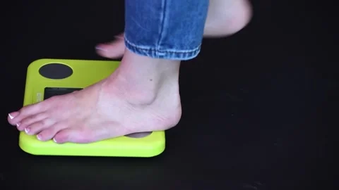Caucasian bare feet standing on scale to measure weight,black background. Contro Stock Footage 248436231
