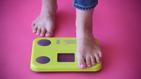 Caucasian bare feet standing on scale to measure weight,pink background. Control Stock Footage 248436236