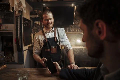 Caucasian bartender smiling at client grateful for support while client pays for Stock Photos
