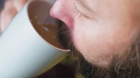 Caucasian bearded man drinking coffee in the kitchen. Close-up of a man with a Video stock 227914090