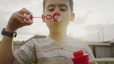 Caucasian boy blowing soap bubbles in the backyard on a sunny evening. Childhood Stock Footage 247032895