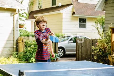 Caucasian Boy Playing Table Tennis In Backyard