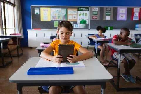 Caucasian boy using digital tablet while sitting on the desk in the class at 스톡 사진