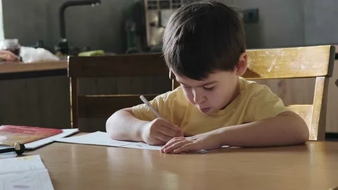 Caucasian boy using a pencil to write in the notebook sitting at the desk in the Stock Footage 194460383