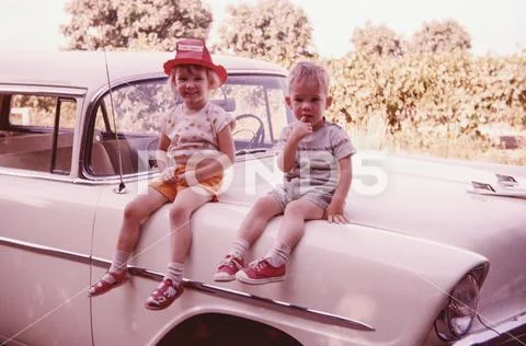 Caucasian brother and sister sitting on vintage car Stock Photos