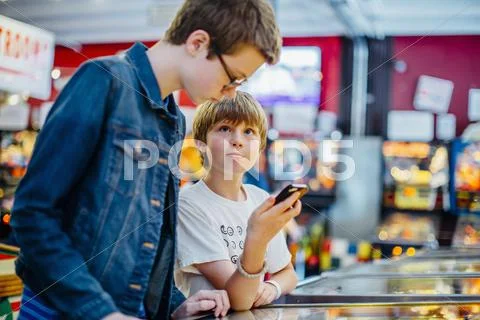 Caucasian brothers using cell phone in arcade Stock Photos